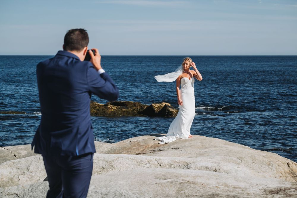 Groom taking a photo of bride at seaside wedding at bull point estate in nova scotia.