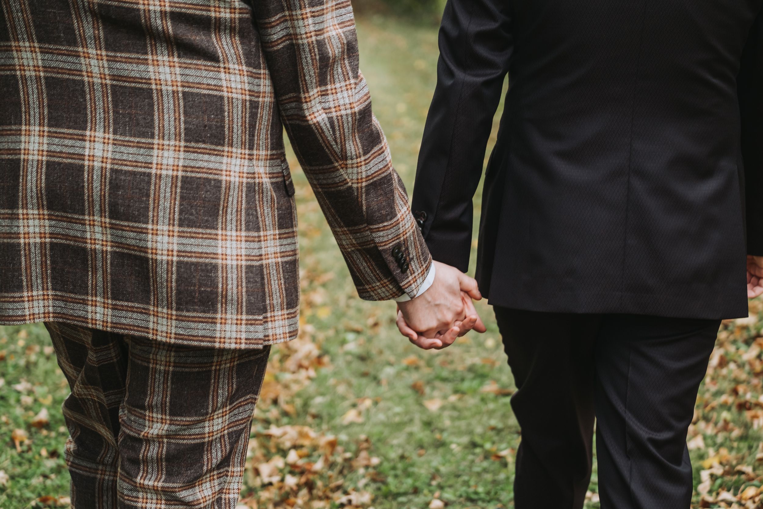 Two grooms wearing suits and holding hands on wedding day.