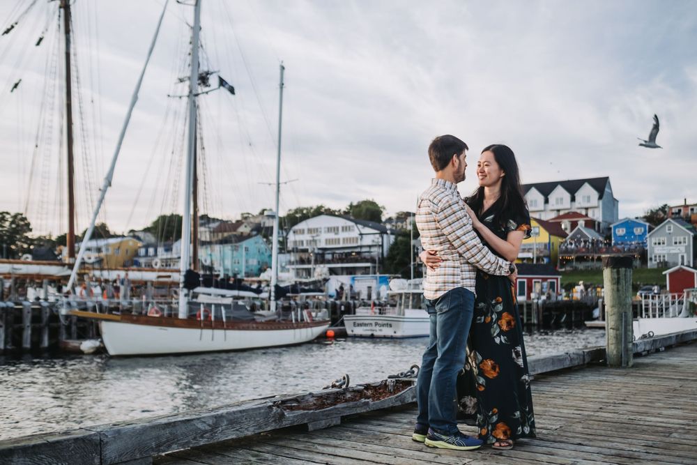 Couple standing on dock with boats in background during Lunenburg Engagement Session.